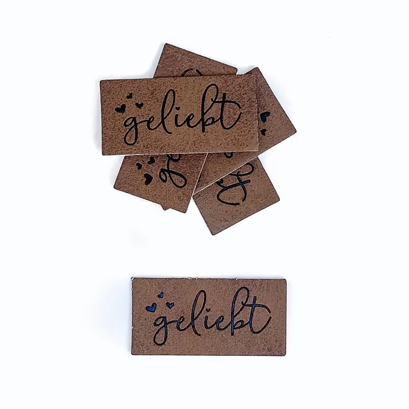 braune Lederlabels mit schwarzer Aufschrift "geliebt" und mit Herzen verziert.